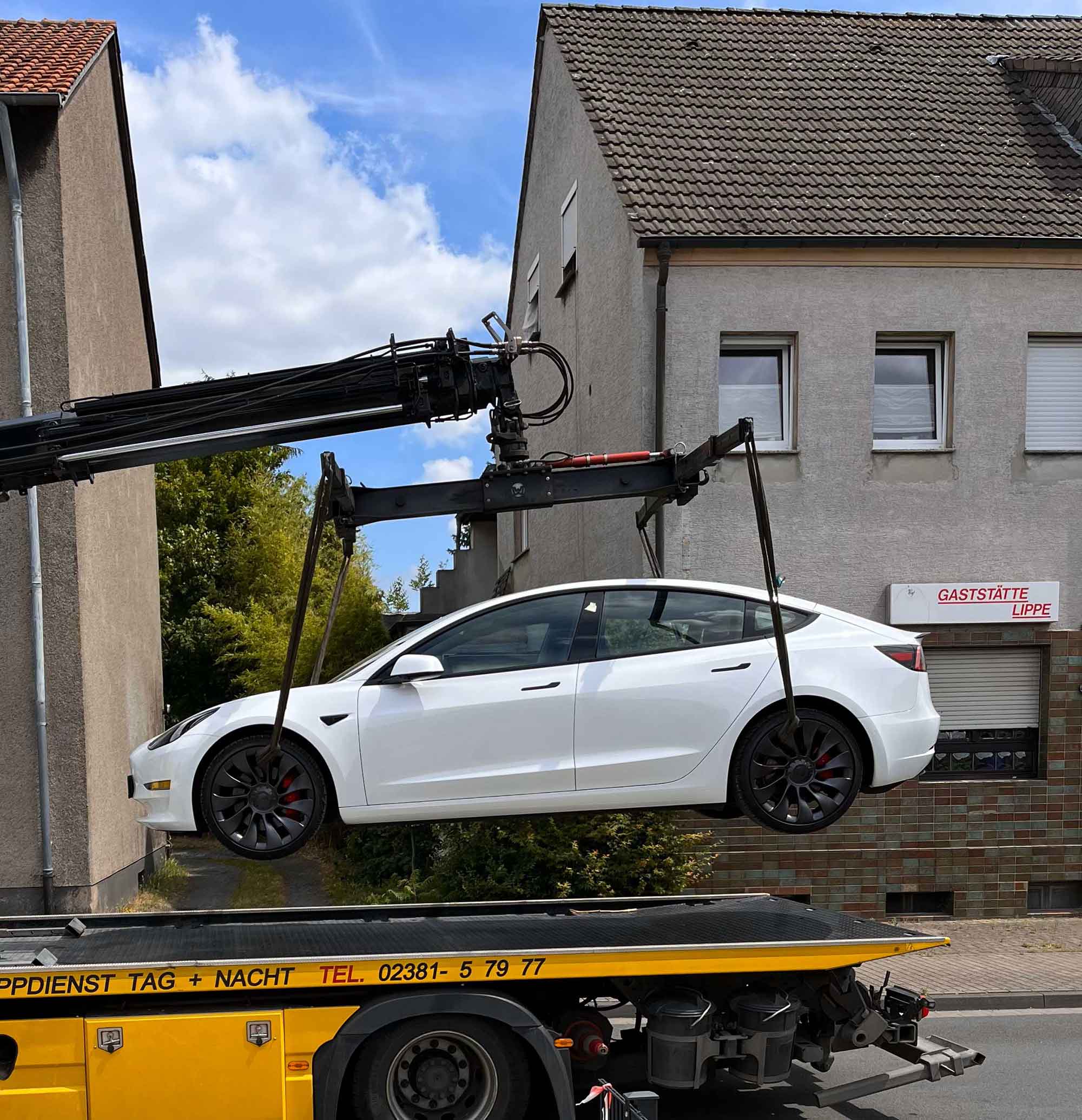 Ein weißes Auto wird von einem Kran auf einen gelben Abschleppwagen gehoben.